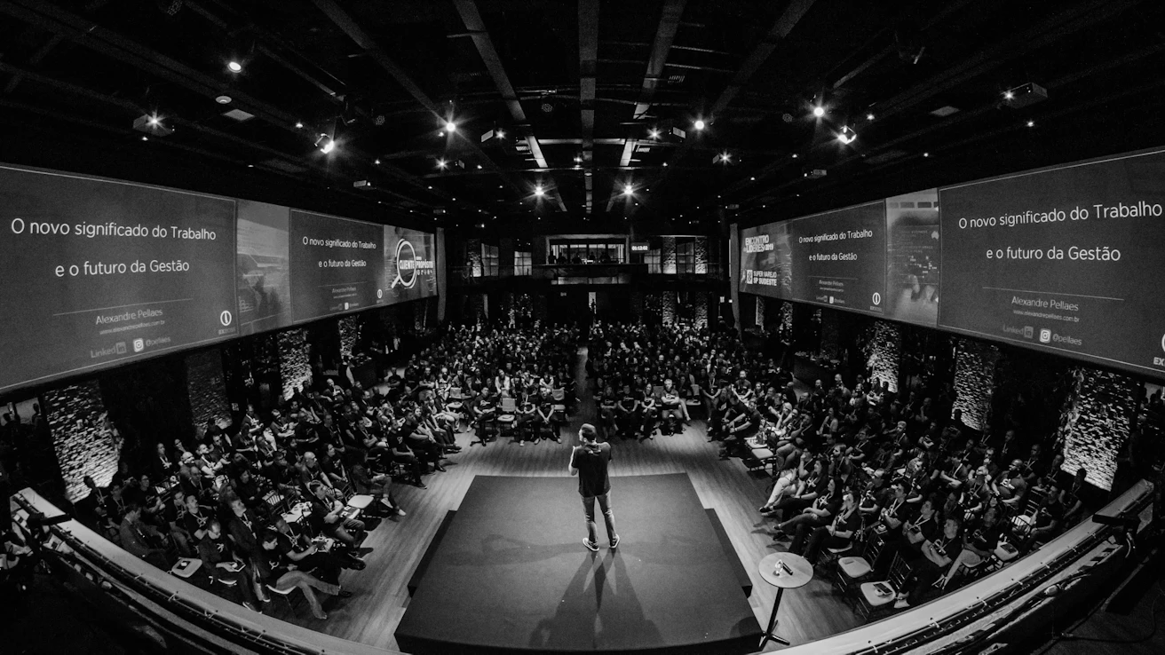 A speaker on a dark stage in front of a full auditorium
