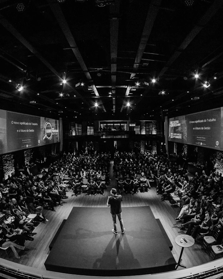 A speaker on a dark stage in front of a full auditorium